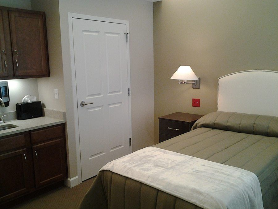A cozy bedroom with a neatly made bed, wall-mounted lamp, and a closed door.