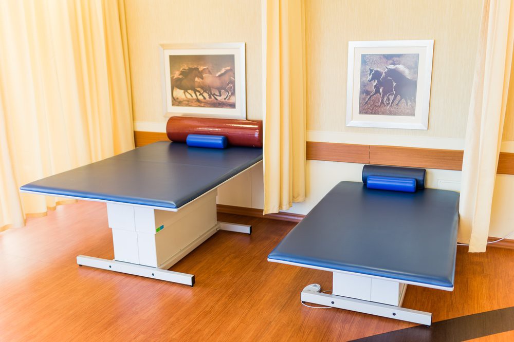 A therapy room with two treatment tables and framed artwork on the walls.