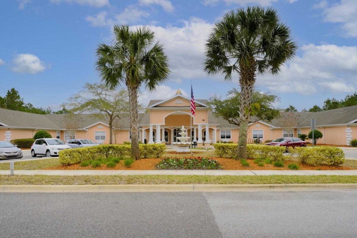 A picturesque view of a building surrounded by palm trees and an American flag under a partly cloudy sky.