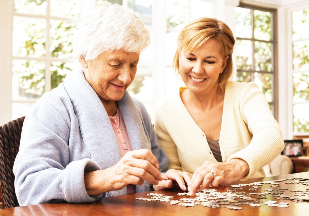 A middle-aged woman and an elderly woman working on a puzzle together at a table.