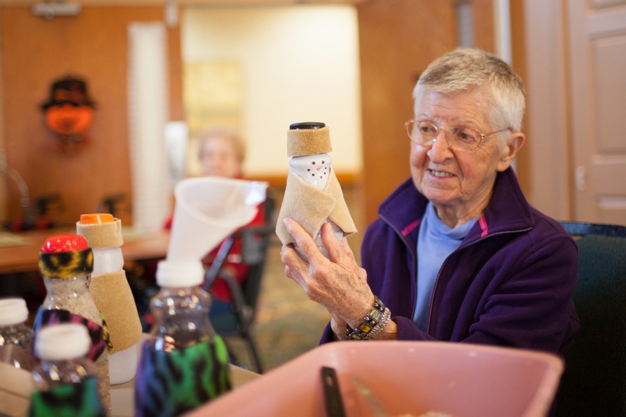 An elderly person engaged in a crafting activity indoors, smiling while holding a handmade item.
