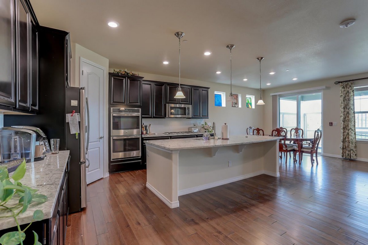 A modern kitchen with an island and pendant lighting, featuring dark cabinetry and hardwood floors.