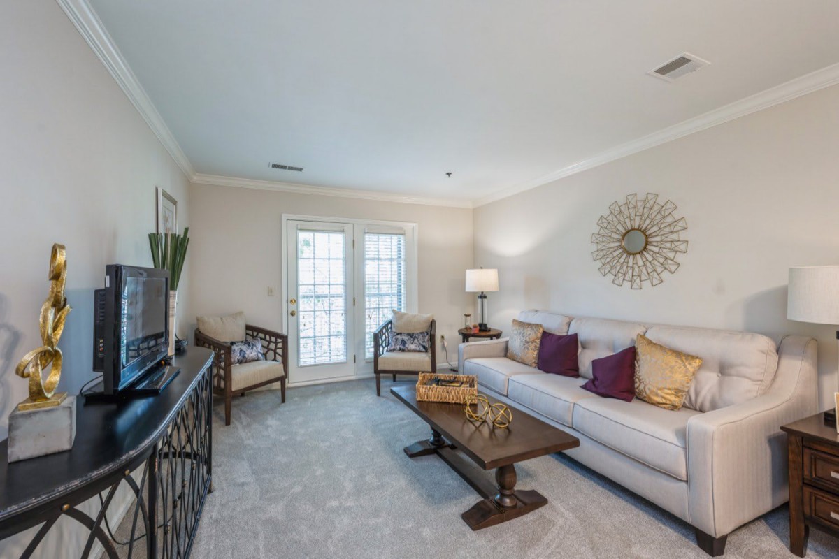 A cozy living room with a stylish interior, featuring a white sofa and decorative pillows, complemented by a wooden coffee table and elegant wall art.