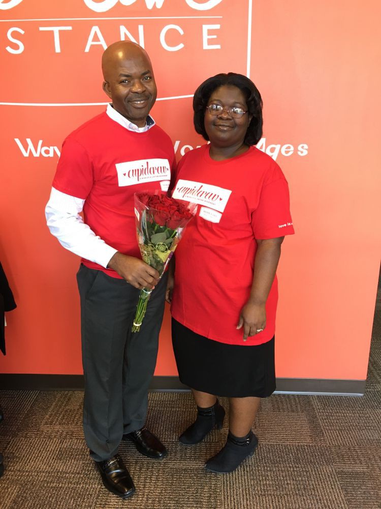 A man and woman smiling, both wearing red shirts, with the man holding a bouquet of flowers.