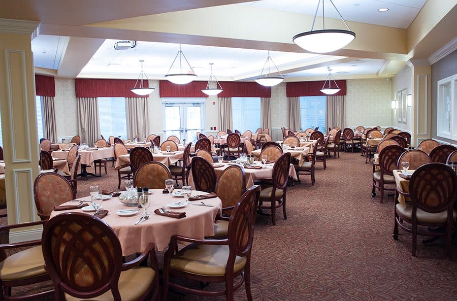 An elegantly set dining room with multiple tables and chairs arranged under chandeliers.