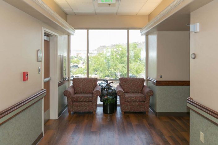 A cozy lounge area with two armchairs and a small table set near a large window, offering a view of greenery outside.