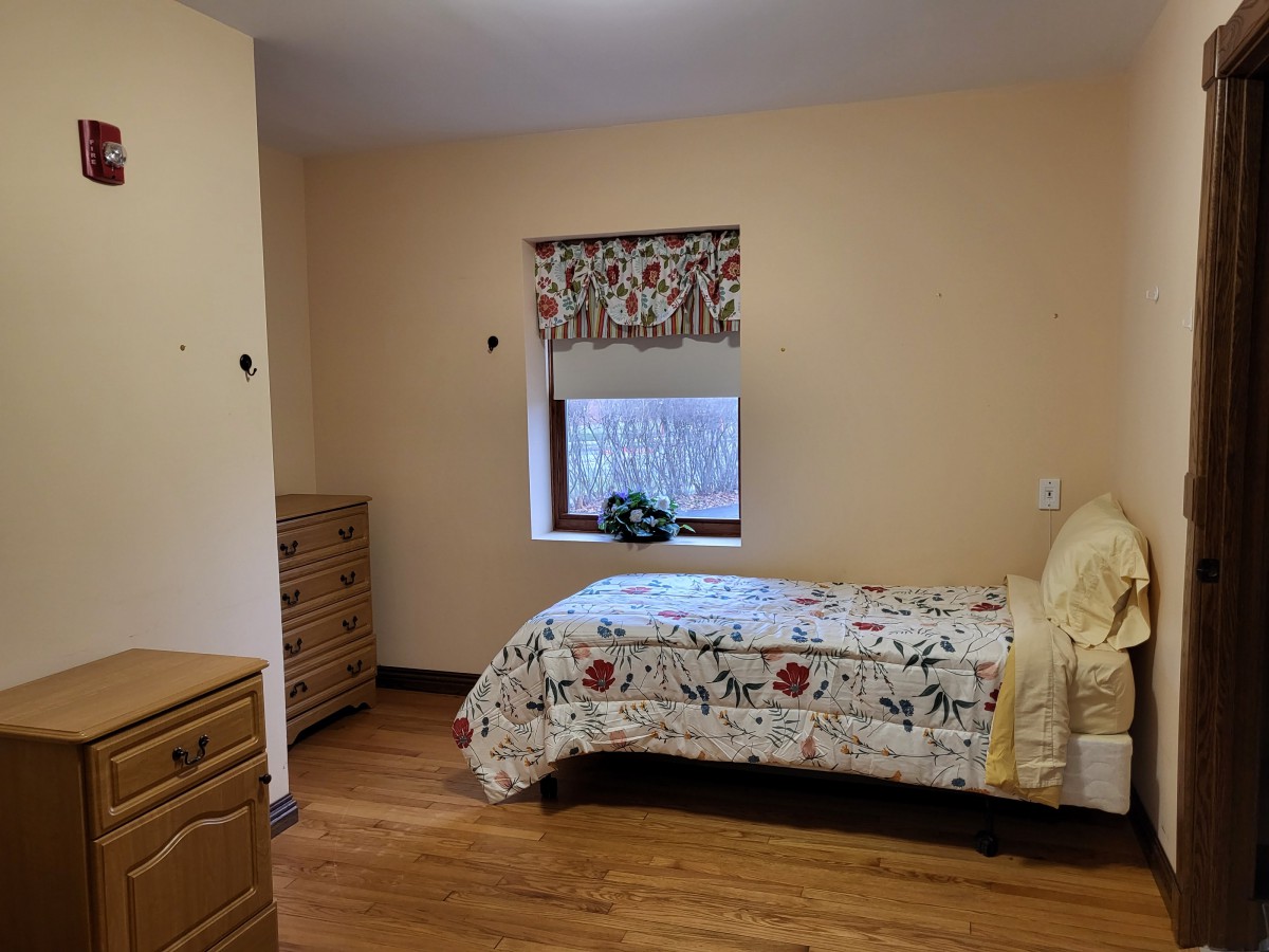A cozy bedroom with a single bed, wooden dresser, and a window with floral curtains.