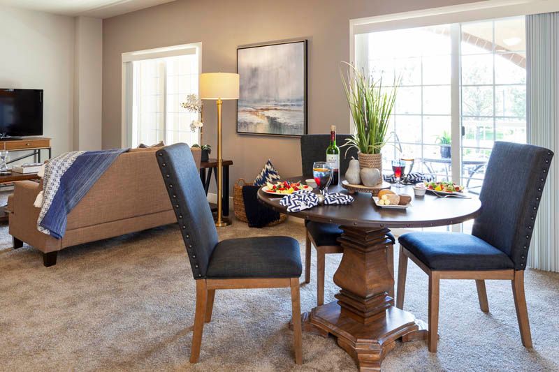 A cozy dining area with a round wooden table set for a meal, adjacent to a comfortable living room with ample natural light.