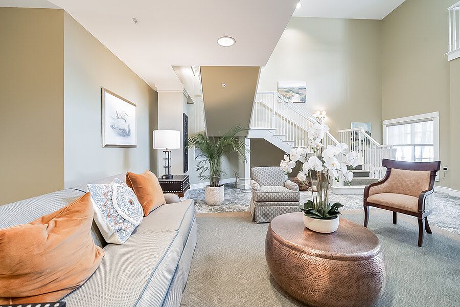 A stylish and modern living room featuring comfortable seating, a round coffee table with floral decor, and a decorative staircase in the background.