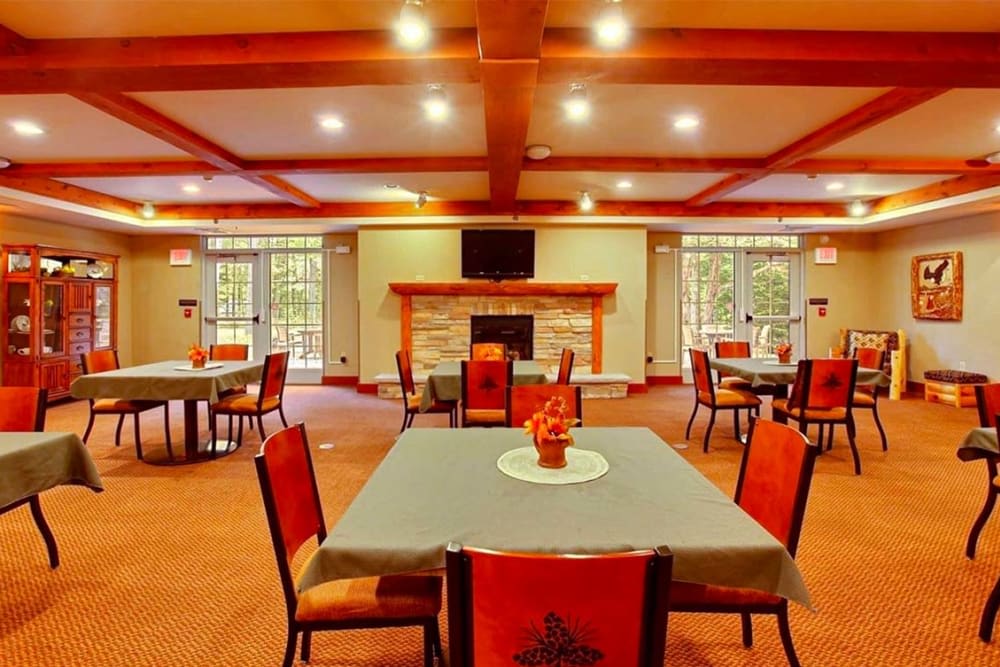 A spacious dining room featuring several tables and chairs, with a central fireplace and warm lighting.