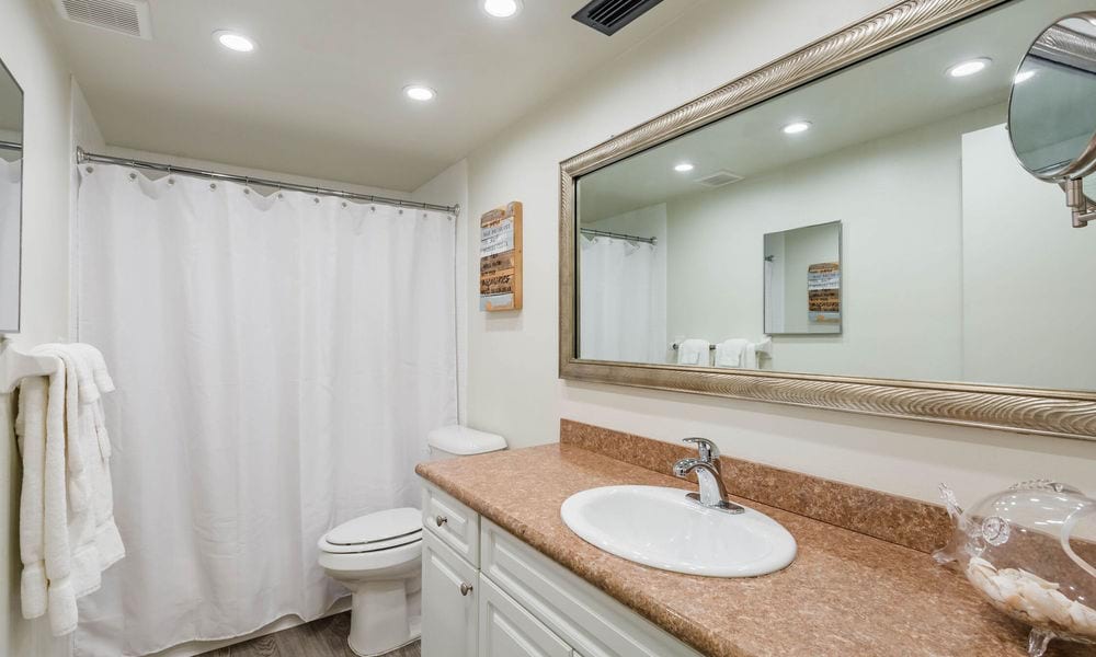 A modern bathroom with a large mirror, countertop sink, and shower curtain.