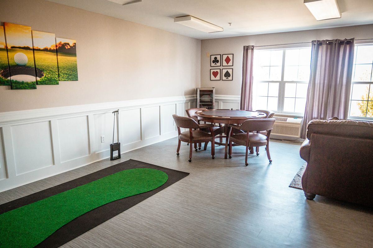 A cozy dining room with a round table and chairs, featuring a golf mat and wall art.