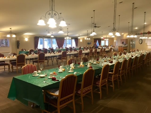 A large dining hall set up for a banquet with decorated tables and chairs under warm indoor lighting.
