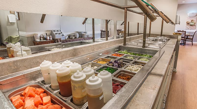 A self-serve salad bar with a variety of fresh vegetables and condiments.