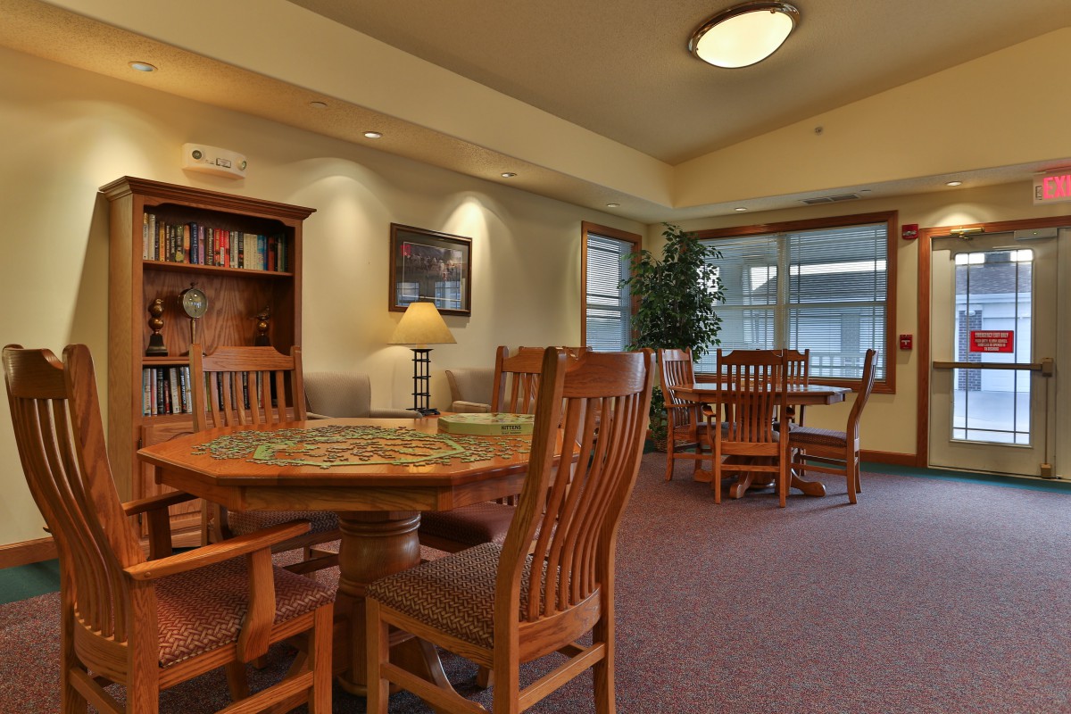 A cozy library reading area with wooden tables and chairs, surrounded by bookshelves.