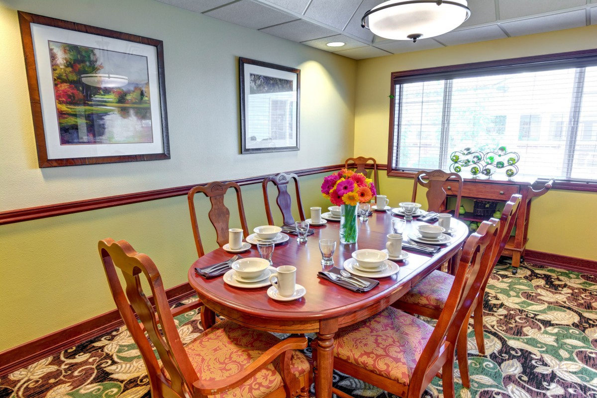A cozy dining room with a table set for a meal, featuring elegant chairs, floral centerpiece, and framed artwork on the walls.