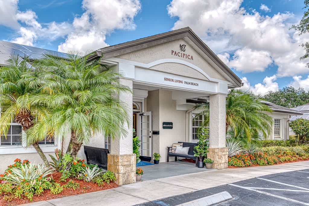 A welcoming building entrance surrounded by palm trees and well-maintained landscaping under a partly cloudy sky.