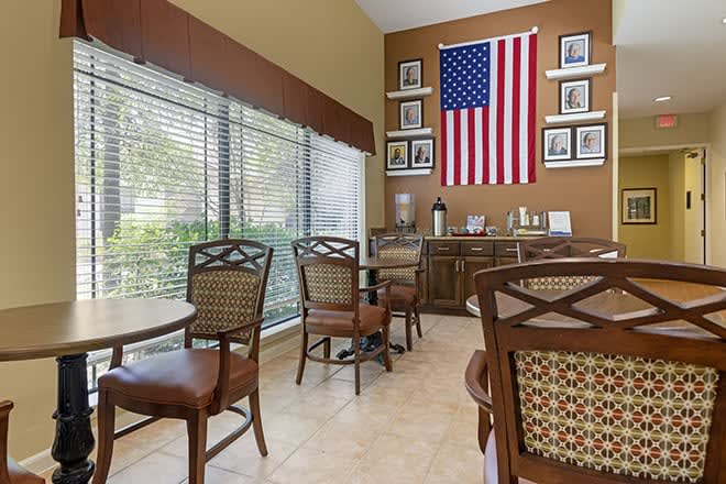 A cozy cafe interior featuring an American flag and several tables and chairs near large windows.