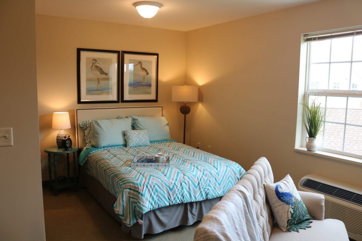 A cozy bedroom with a neatly made bed, framed artwork, and ambient lighting.