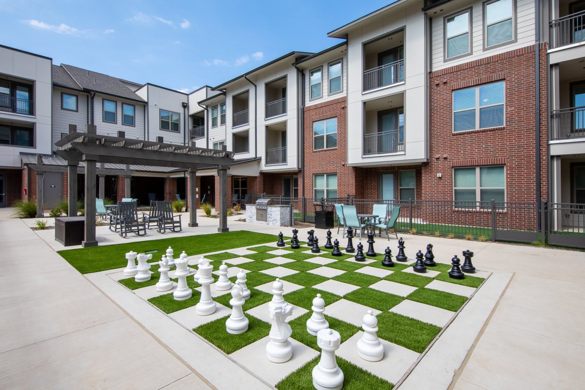 A modern apartment courtyard featuring a giant chess set on a lawn.