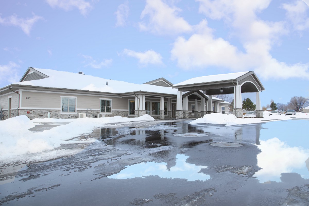 A building with a snow-covered roof and driveway on a cloudy winter day.