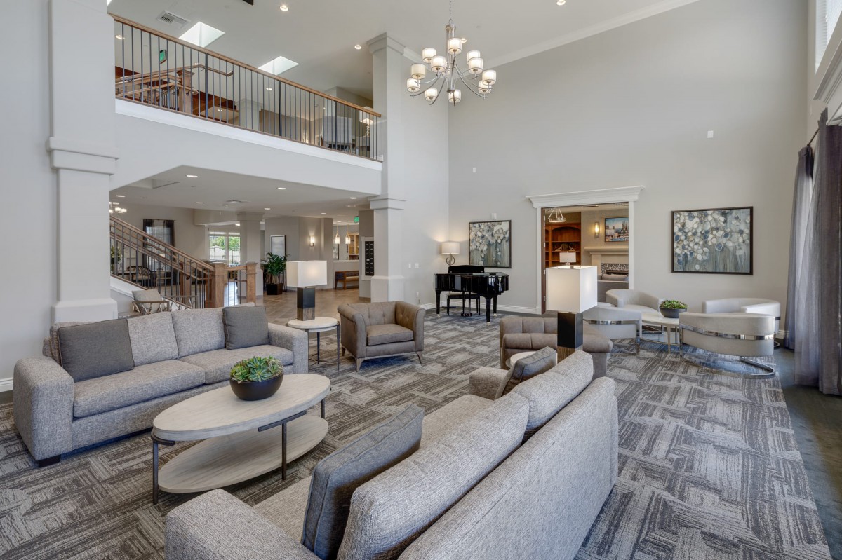 A spacious and elegantly designed living room with modern furniture, a grand piano, and a chandelier.