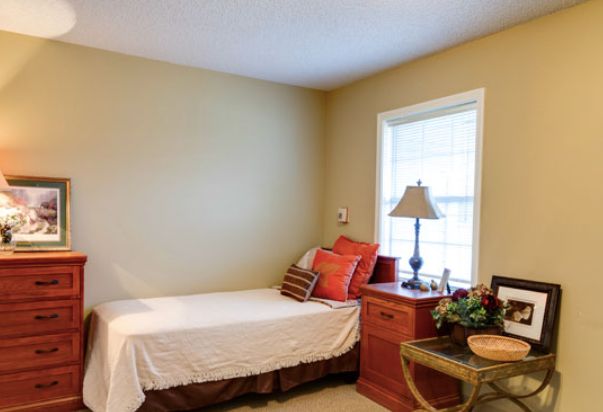 A cozy bedroom with a single bed, colorful pillows, and a wooden nightstand by the window.