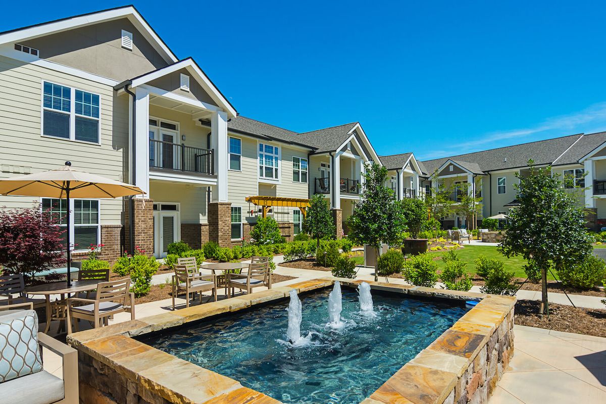 A modern apartment complex with a landscaped courtyard and fountain under a clear blue sky.