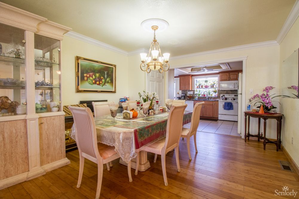 A dining area with a table set for a meal, featuring a chandelier and adjoining kitchen.
