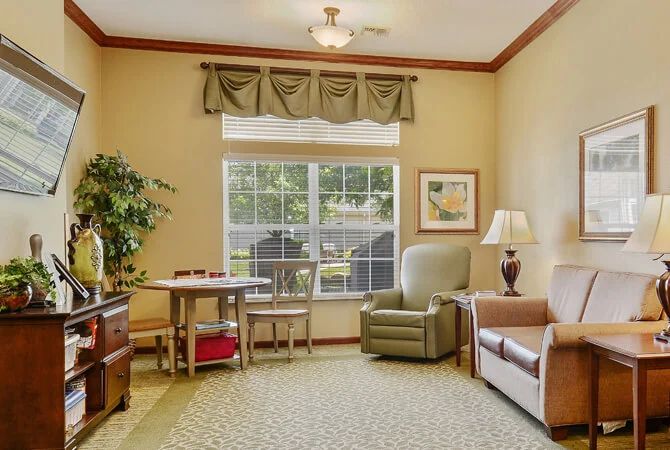 A cozy living room with a large window, armchair, sofa, small table, and decorative plant.