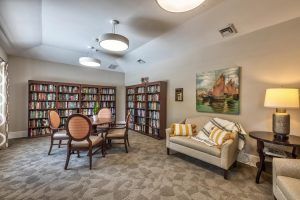 A cozy library reading room with bookshelves, a sofa, chairs, and a table.