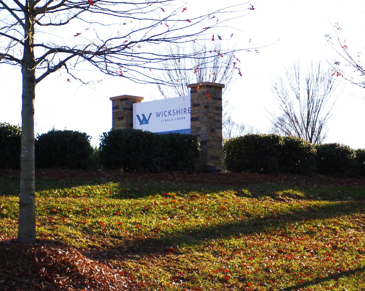 A sign on a grassy landscape with trees in the background.