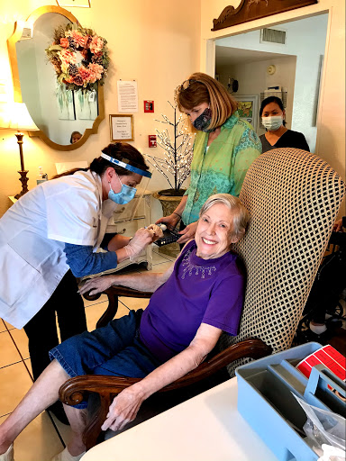 Healthcare workers assist an elderly resident during a vaccination event.