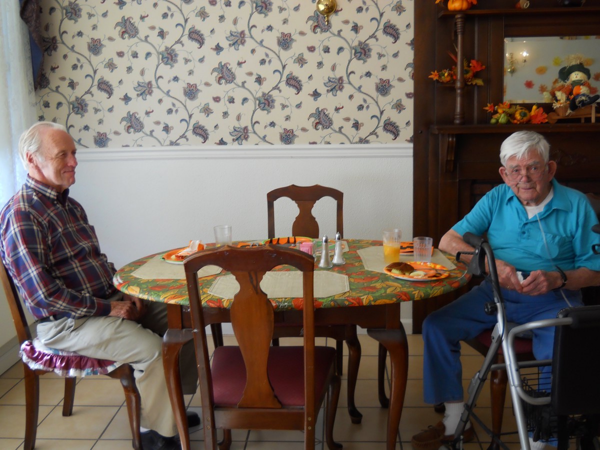Two people sitting at a dining table in a room with floral wallpaper.