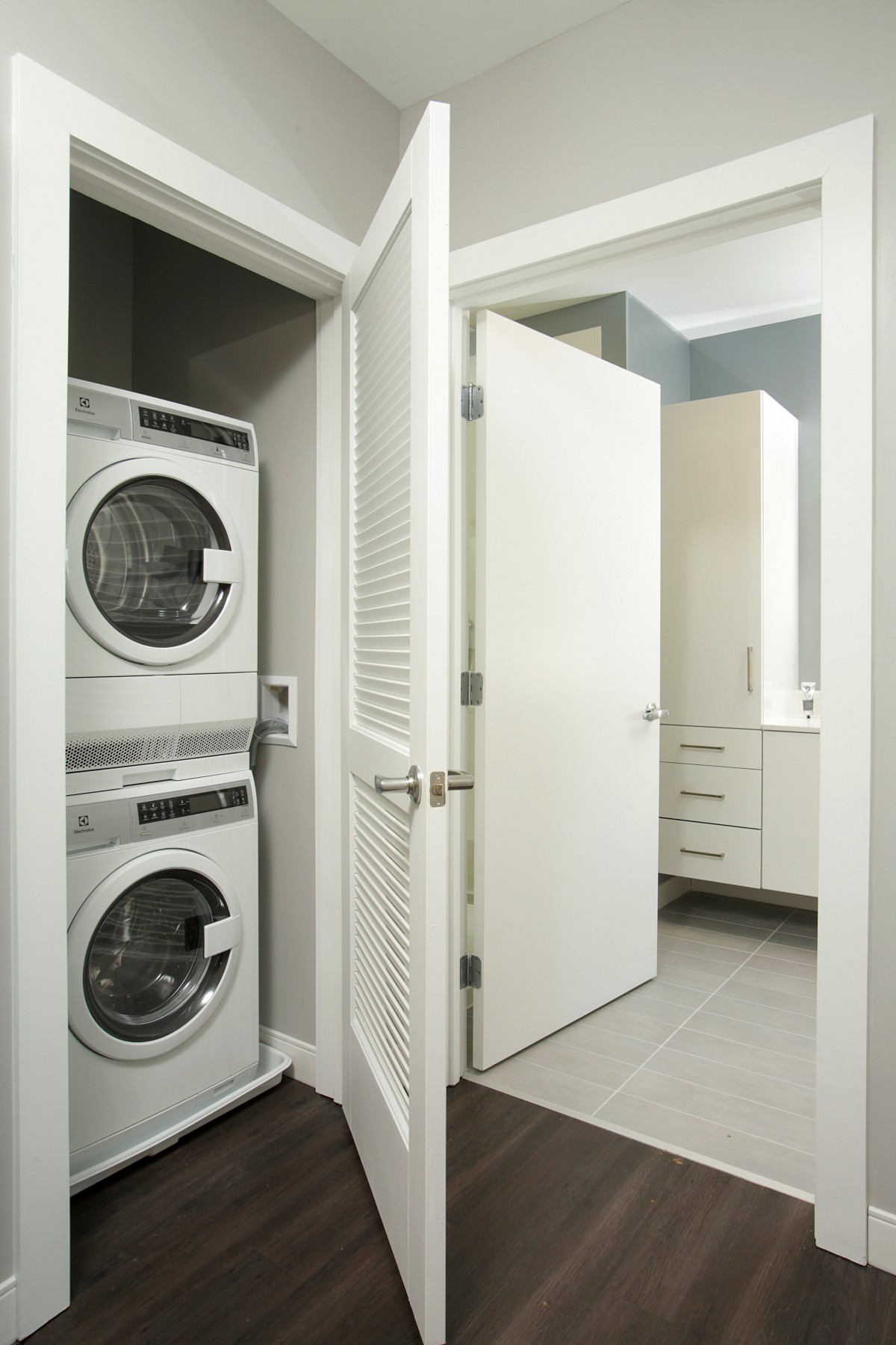 A modern laundry area featuring a stacked washer and dryer next to a bathroom with white cabinetry.