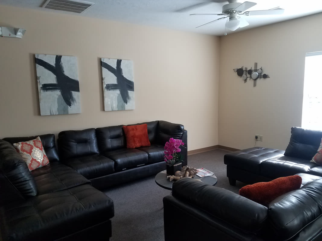 A modern living room with black leather sofas, abstract wall art, and a ceiling fan.