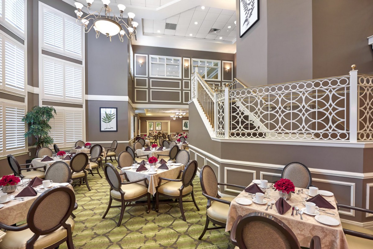 An elegant dining area with stylish tables and chairs, featuring a grand chandelier and decorative staircase.