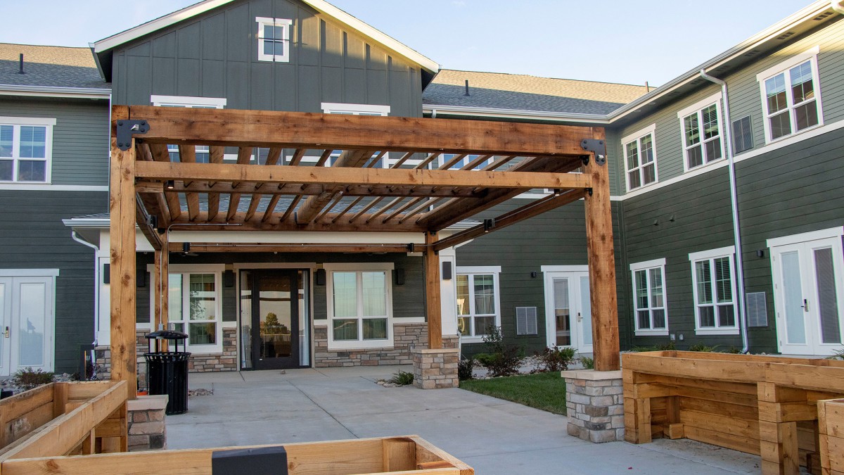 A modern residential building featuring a wooden pergola in its front yard.