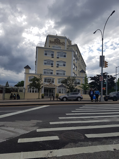A view of a multi-story building under a cloudy sky, with pedestrians crossing the street.