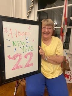 A person smiling while holding a 'Happy New Year 22' sign indoors.