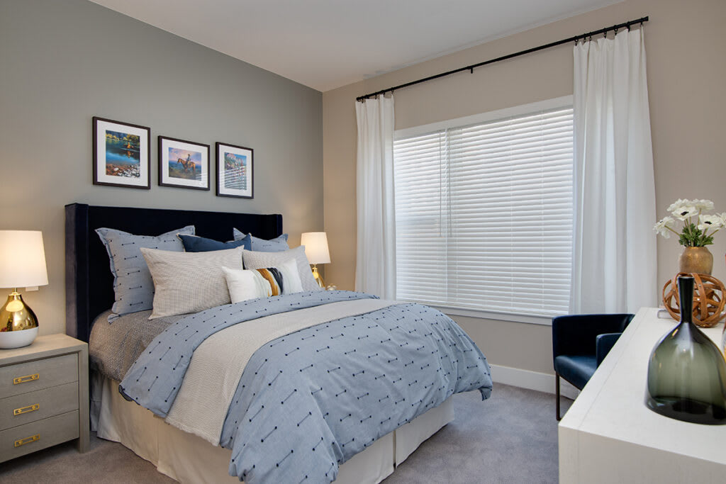 A cozy, modern bedroom with light blue and white bedding and a large window.