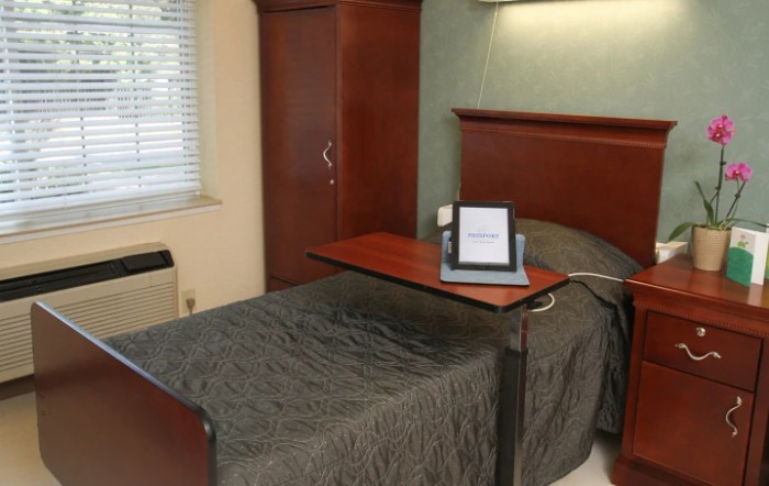 A hospital room featuring a single bed, wooden wardrobe, and overbed table.