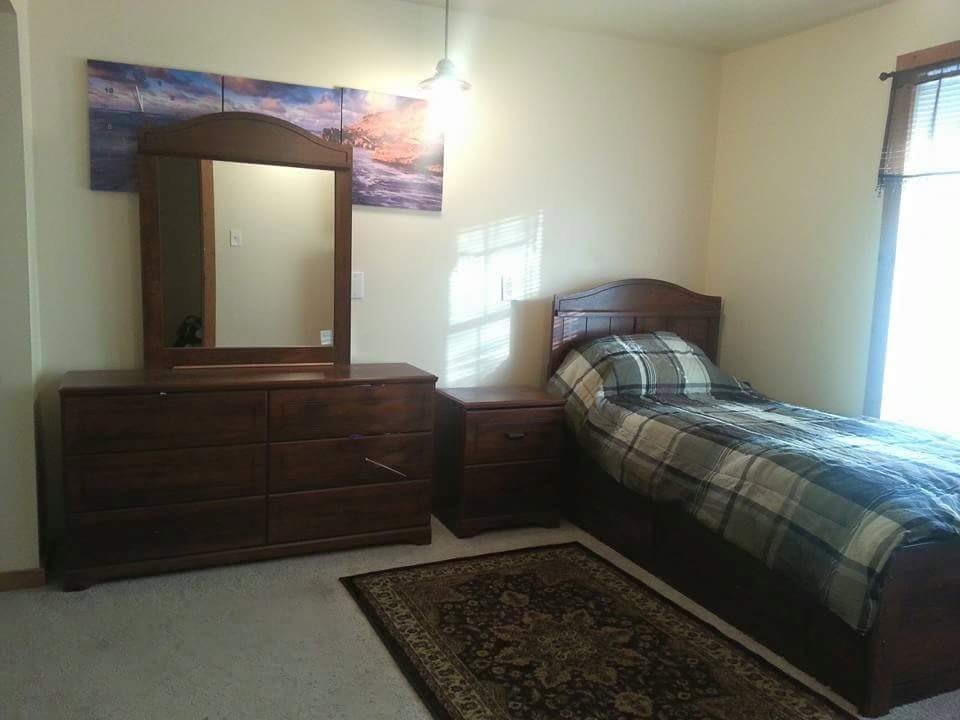 A cozy bedroom featuring a single bed, dresser with mirror, and a decorative rug.