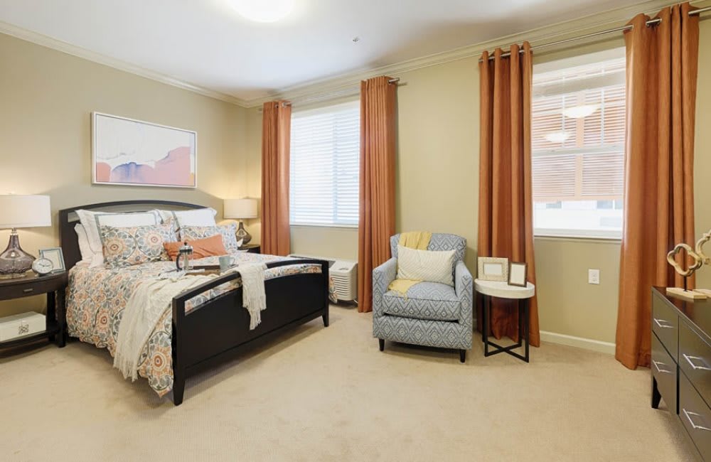 A cozy bedroom with a bed, armchair, and warm-toned curtains.