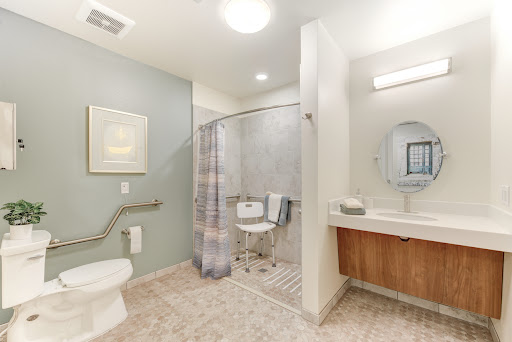 A modern and accessible bathroom featuring a shower, toilet, and sink with a light color scheme.