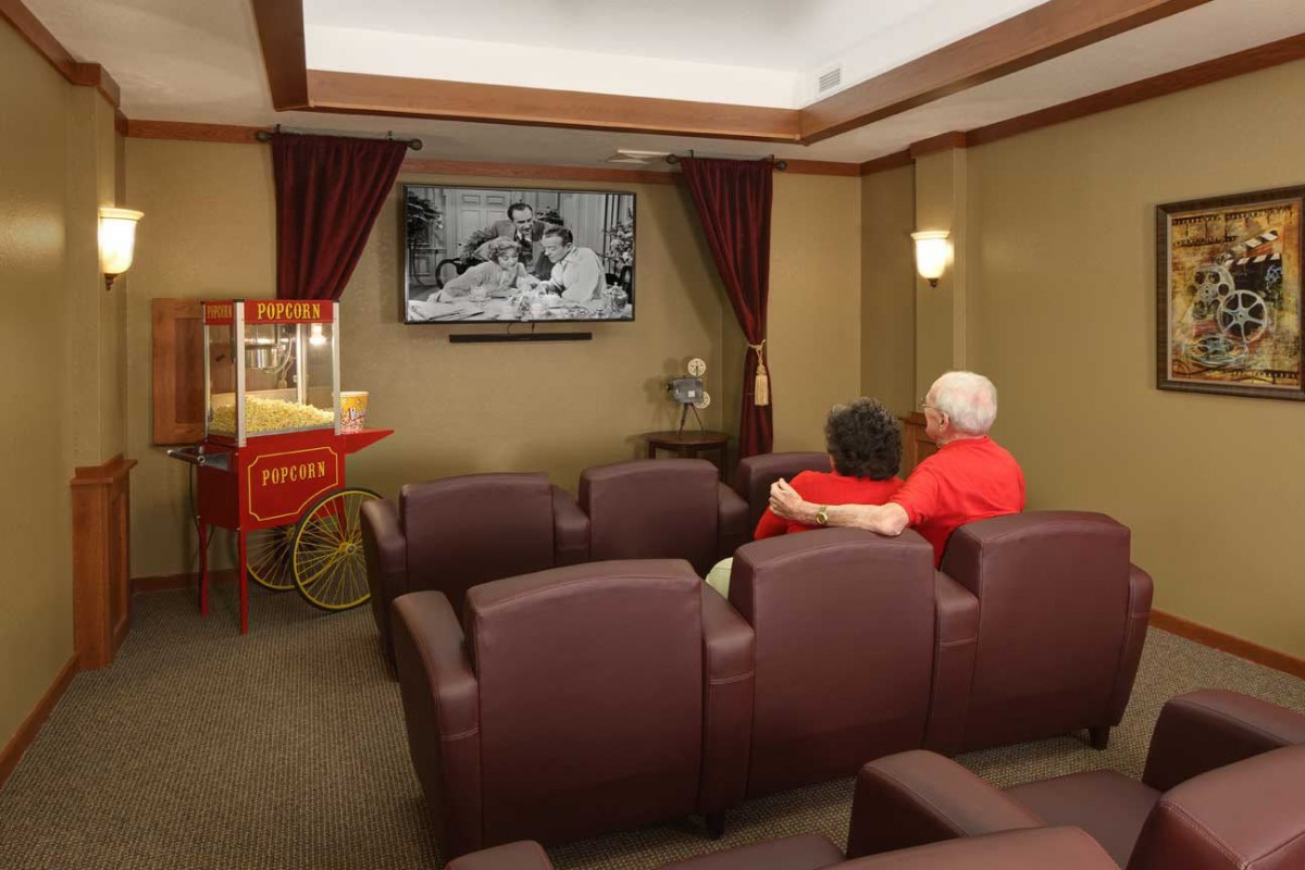 A couple enjoys a black and white movie in a cozy home theater with comfortable seating and a popcorn machine.