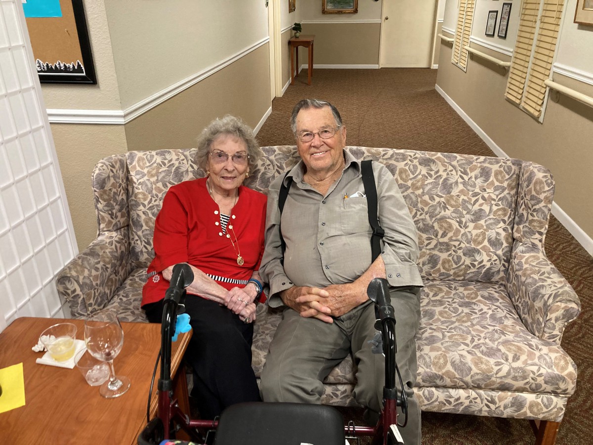 An elderly couple sitting together on a couch, smiling.