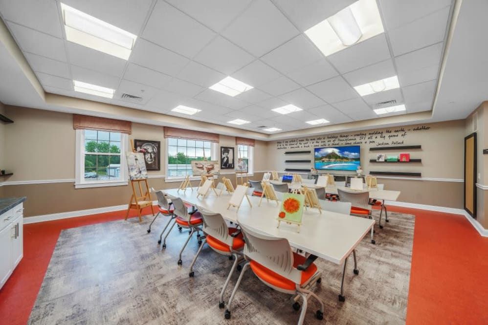 A well-lit and organized classroom featuring tables, chairs, bookshelves, and large windows.