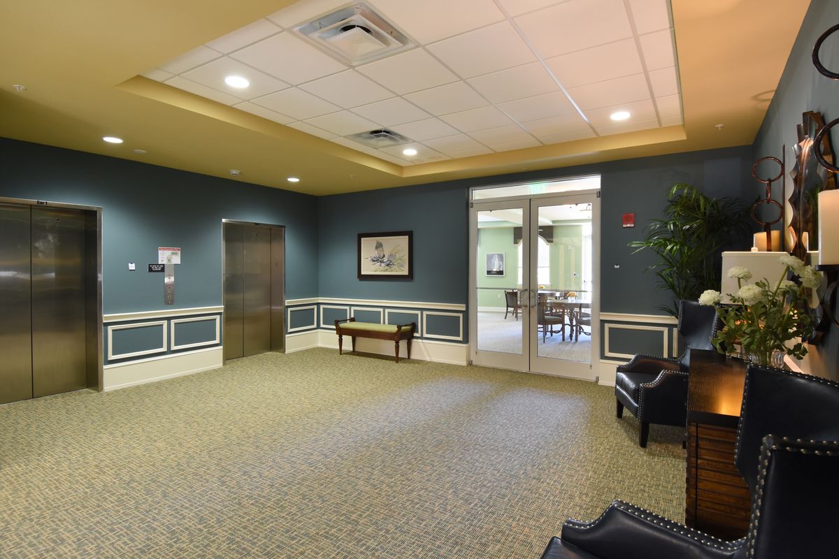 A spacious waiting room with blue walls and carpet flooring, featuring a bench and a doorway leading to another room.