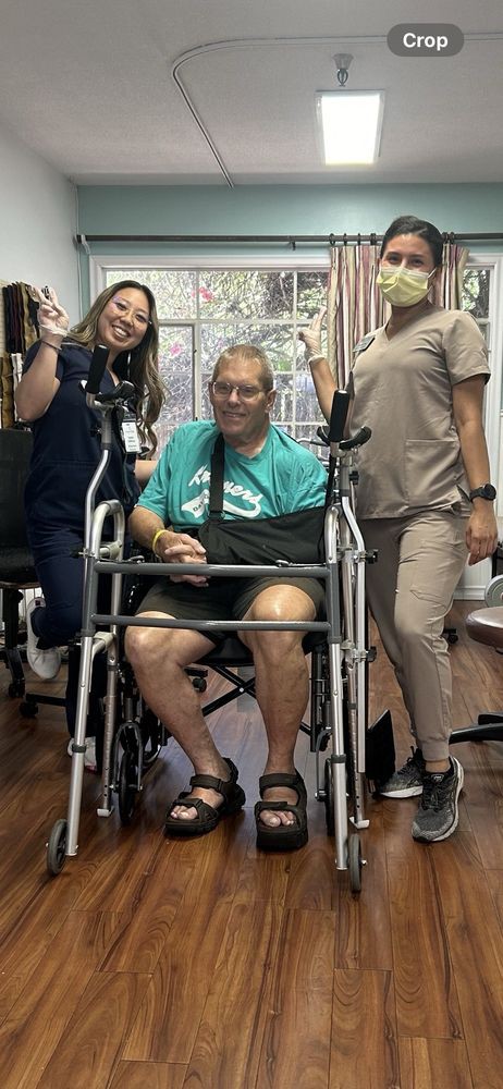 A patient in a wheelchair poses with two hospital staff members, all smiling indoors.